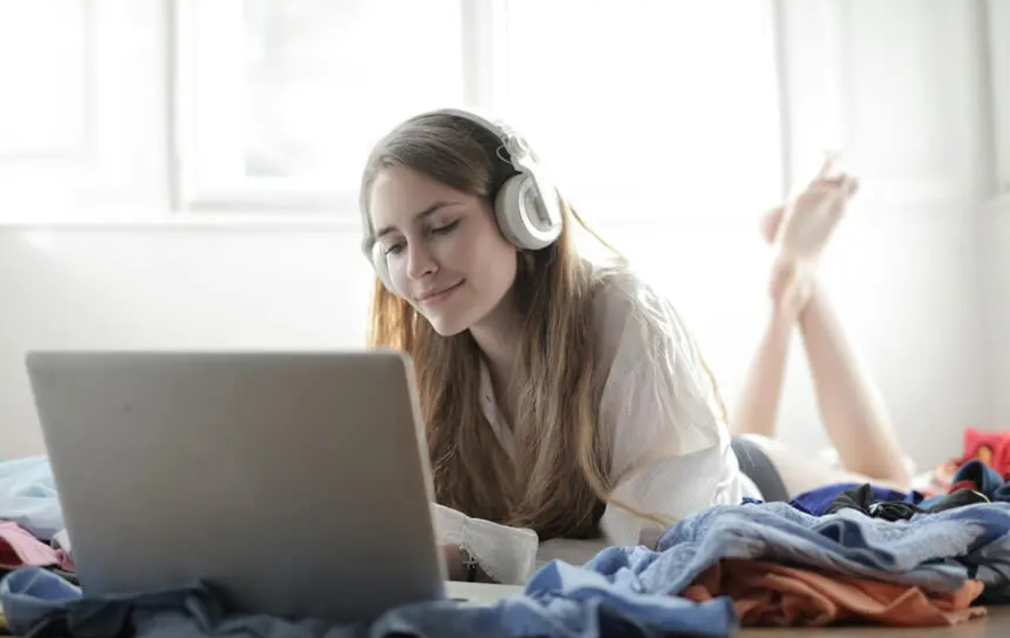 Joven escuchando música o viendo contenido de streaming en España mientras usa auriculares y un portátil sobre una cama