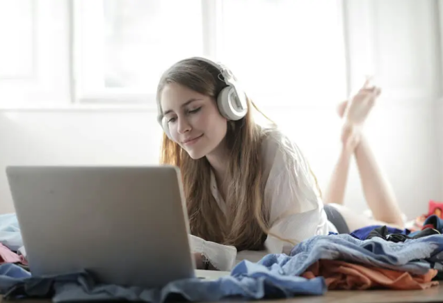 Joven escuchando música o viendo contenido de streaming en España mientras usa auriculares y un portátil sobre una cama